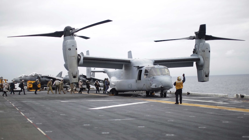 Military personnel board a helicopter on the deck of an aircraft carrier.