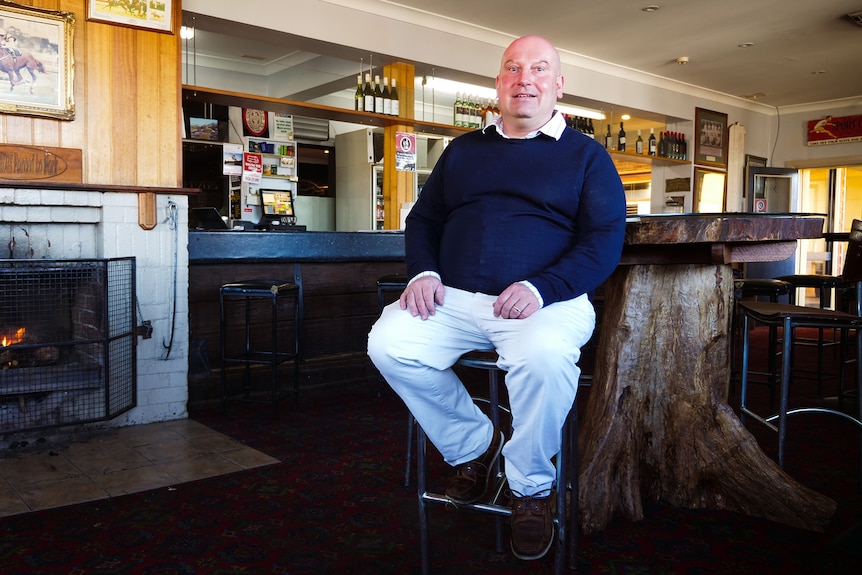 A man sits in a bar with a fireplace in the corner