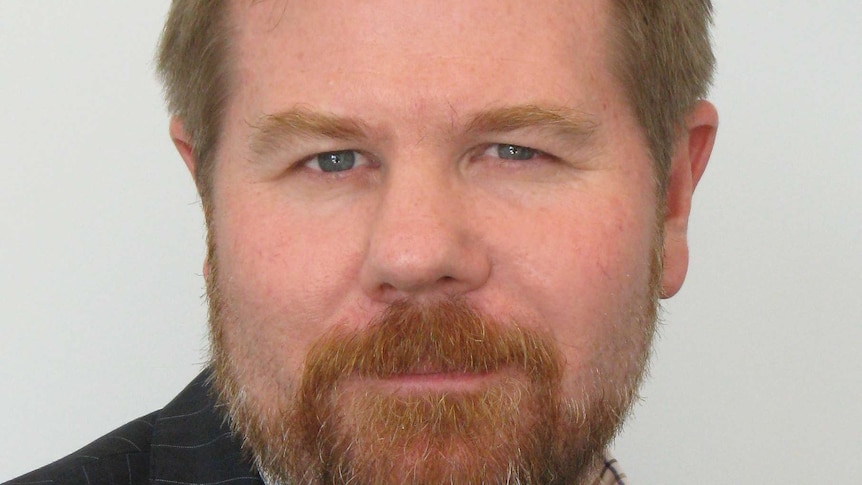 David Kilcullen has strawberry blonde hair, moustache and beard, blue eyes and is looking directly at the camera