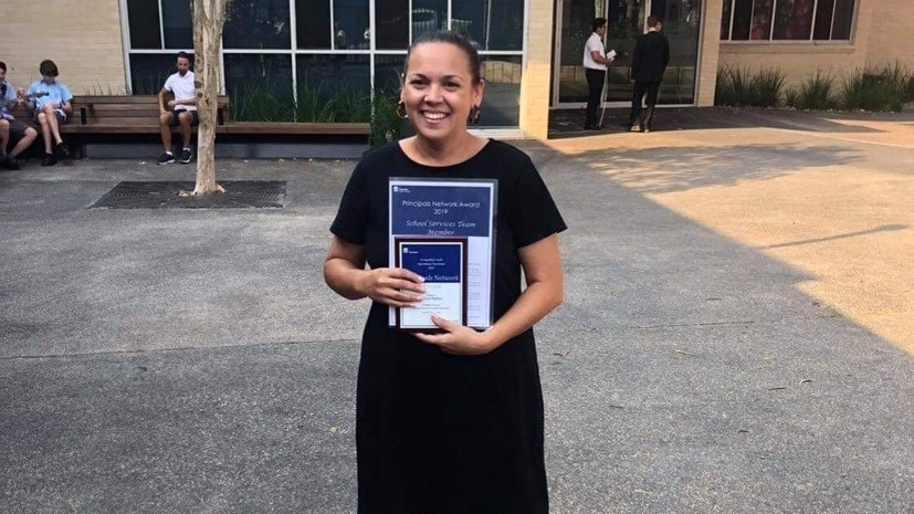 woman wearing black dress holds up an award at school