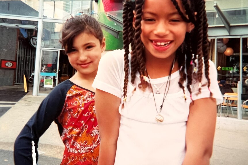 Two children are seen in front of a shopping centre and posing for the camera, smiling.