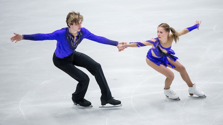 A figure skating pair hold hands as they build up speed moving across the ice.