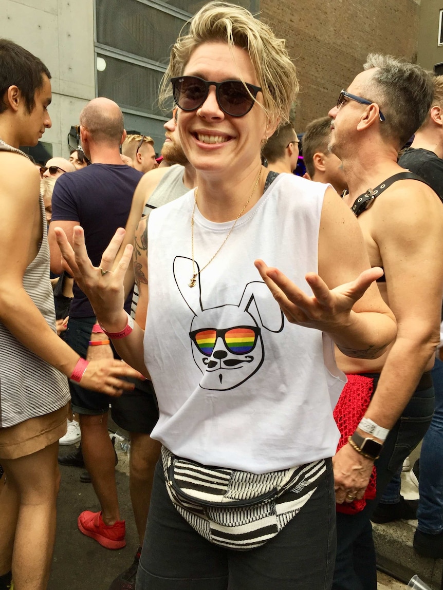 A woman with short blonde hair and sunglasses smiling to camera at a laneway party.