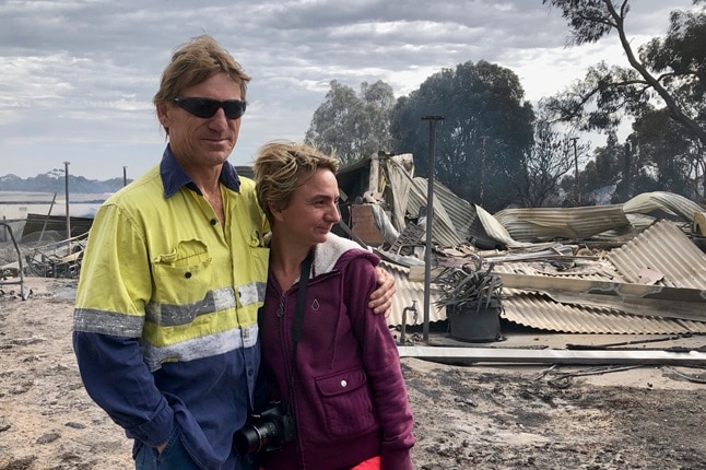 Two people stand near their destroyed house.