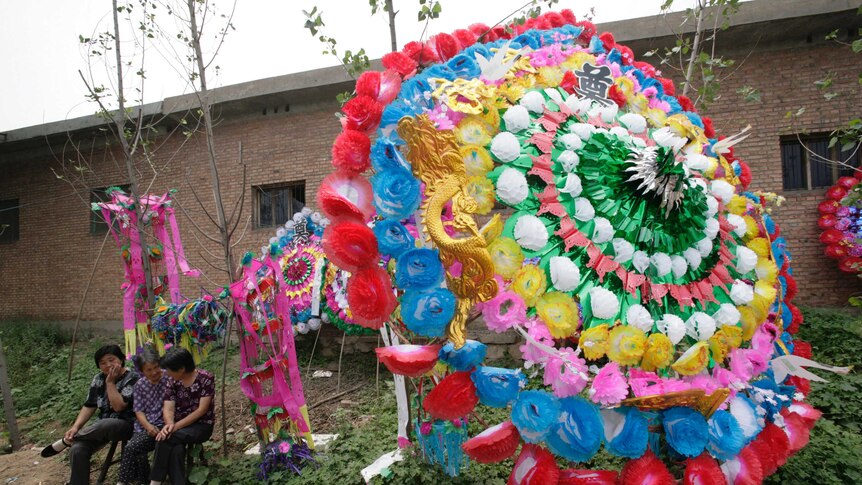 Villagers sit beside a funeral wreath outside the funeral tent during a traditional rural Chinese funeral