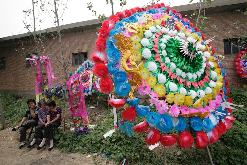 Villagers sit beside a funeral wreath outside the funeral tent during a traditional rural Chinese funeral