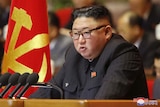 North Korean leader Kim Jong-un sits in front of a row of microphones and next to a North Korean flag.