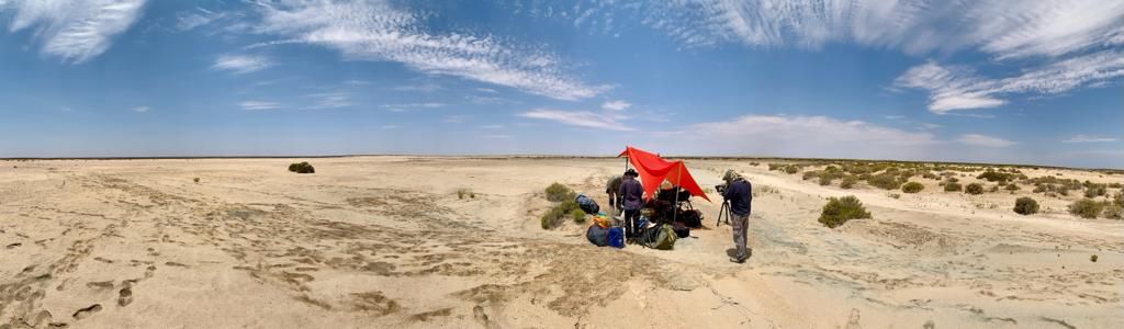 A flat open dessert with a film crew filming something on the right under a red tent-like structure