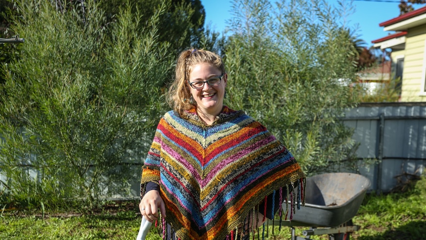 A woman in colourful clothes in her backyard leaning on a gardening tool.