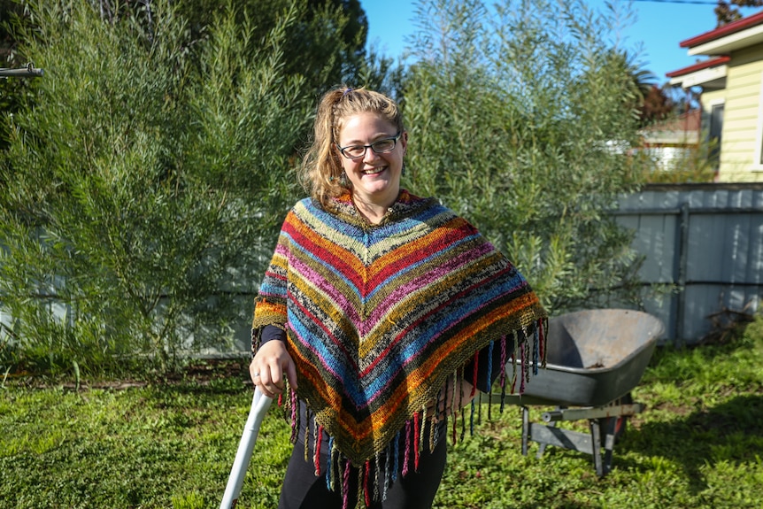 A woman in colourful clothes in her backyard leaning on a gardening tool.