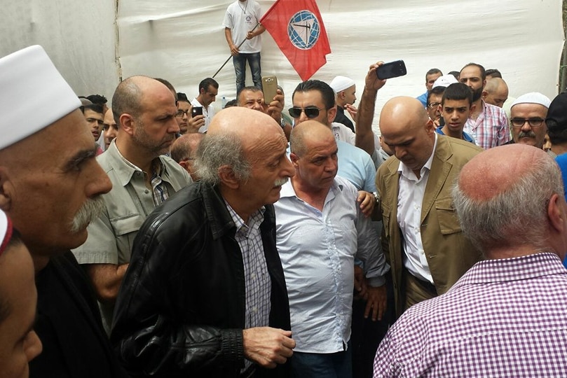 Walid Jumblat walks with supporters, a flag of his party is in the background