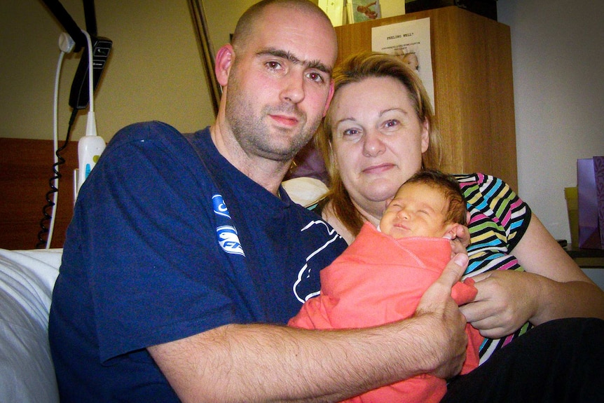 Two parents hold a newborn baby in hospital.