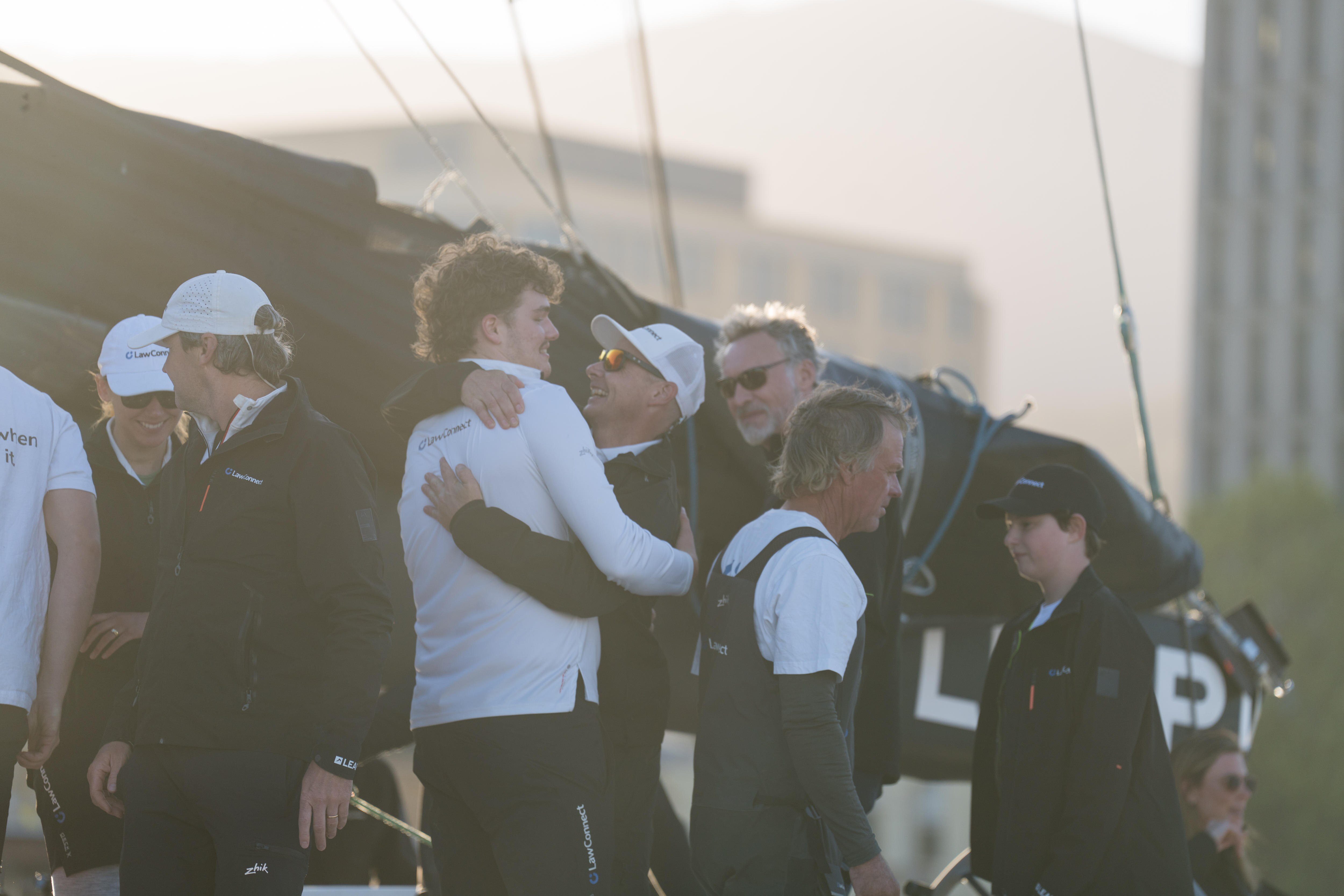 Crew members hug on board a sailing boat.