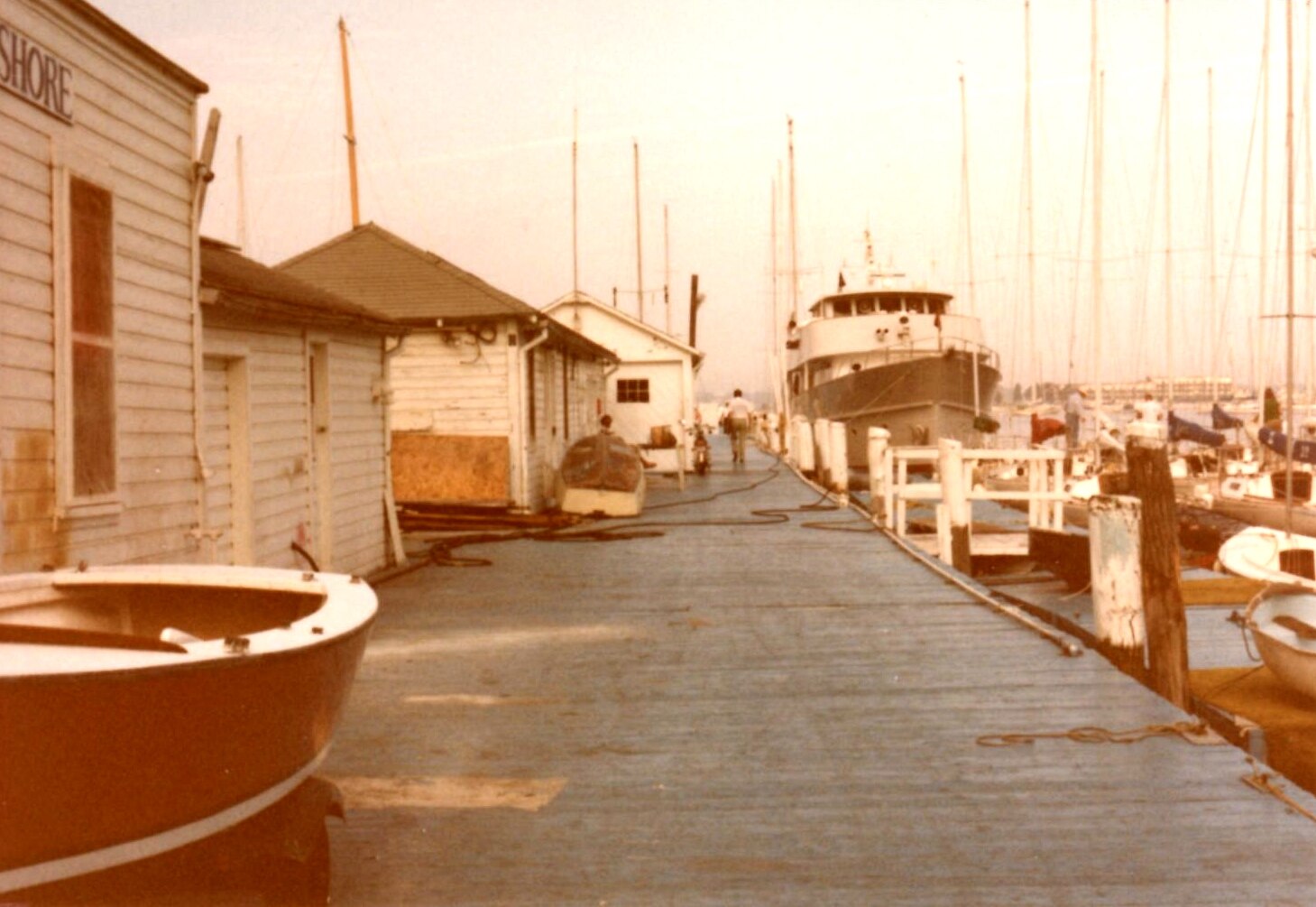 Weatherboard buildings on a dock with many yachts moored along it.