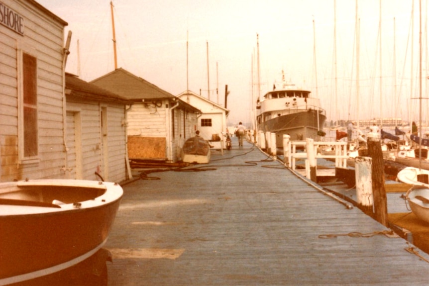 Weatherboard buildings on a dock with many yachts moored along it.