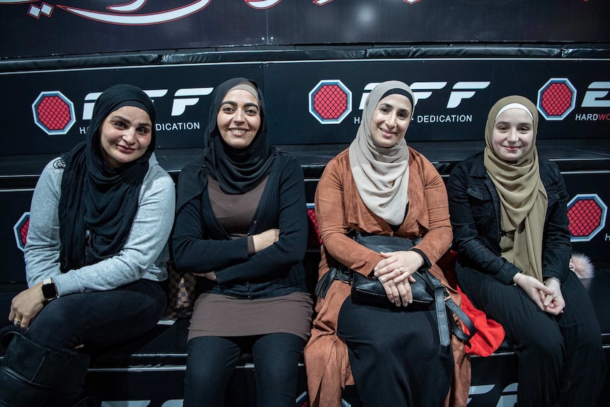 Four women sit on a bench at a gym.