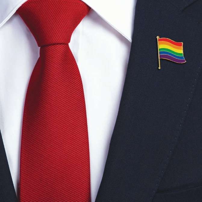 close up of navy suit and red tie, with rainbow flag pin on the collar
