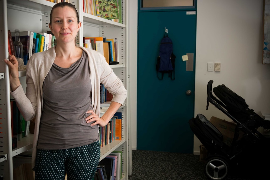 A woman stands next to a bookshelf with childcare accoutrements in the background