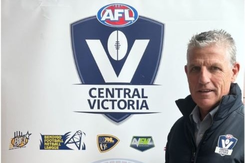 A man with grey hair stands in front of a sign