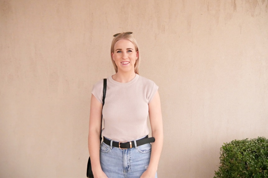 Young woman wearing beige top and jeans smiles at camera