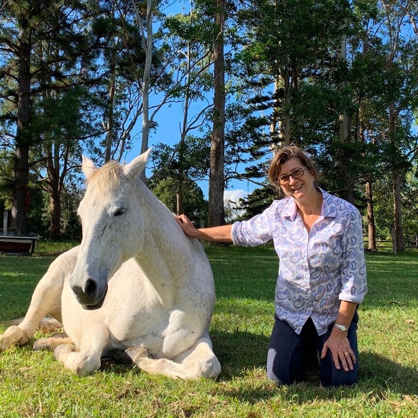 Tyra the rescue mare and her carer Candida Baker are sitting down in a paddock.