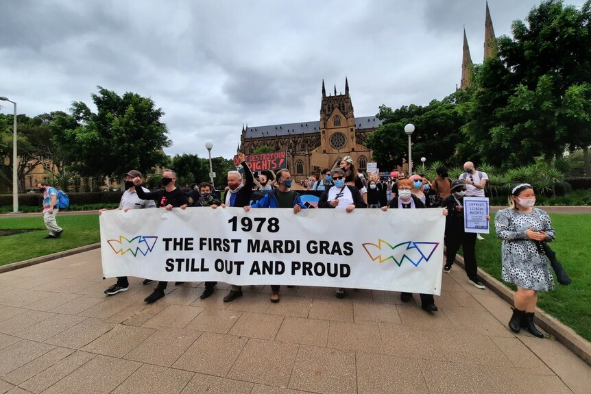 A group of older people marching with a large banner that reads 1978 the first Mardi Gras still out and proud.