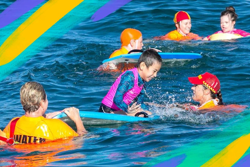 Three kids in bright coloured swimwear in the ocean near the beach with adults helping them learn to swim