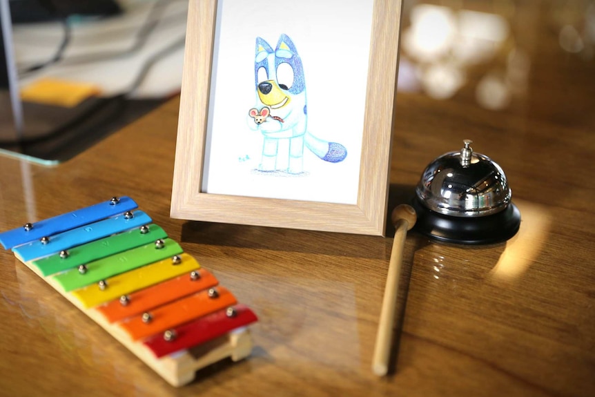 A desk with a coloured sketch of Bluey, a xylophone and a bell.