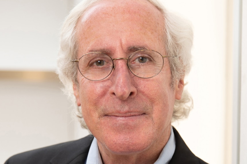 Bruce Wolpe poses for a formal headshot wearing a dark jacket and pale blue shirt