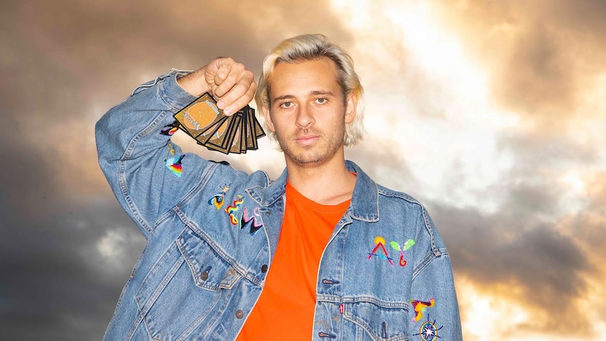 A photo of Flume holding up a hand of Magic: The Gathering guards against a cloudy sky