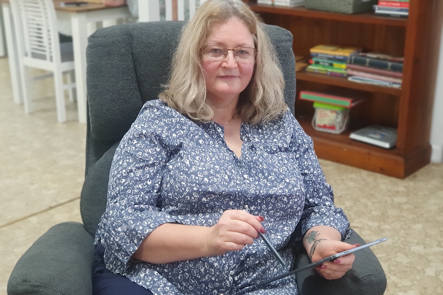 a woman sitting on a chair looking at a centrelink website on her ipad