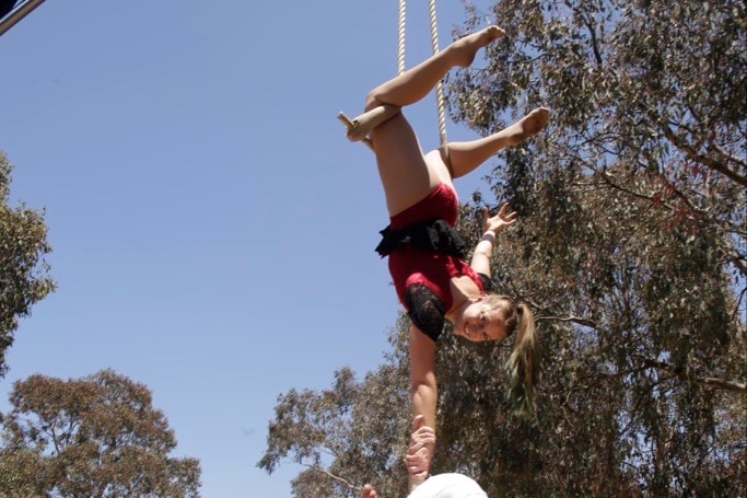 A woman hanging in mid air from a bar behind her knees.