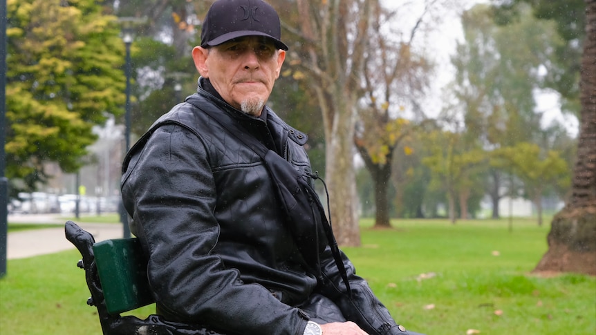 A man in a jacket sits on a park bench.