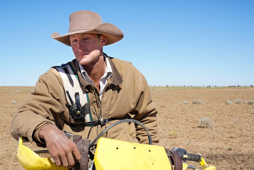 Drover John Sylvester is moving cattle down into the channel country, he is perched on his motorbike.
