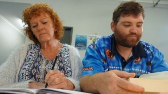 Carol Quinn, left, looks down at a book next to Andrew Moorhead, right, who is doing the same.