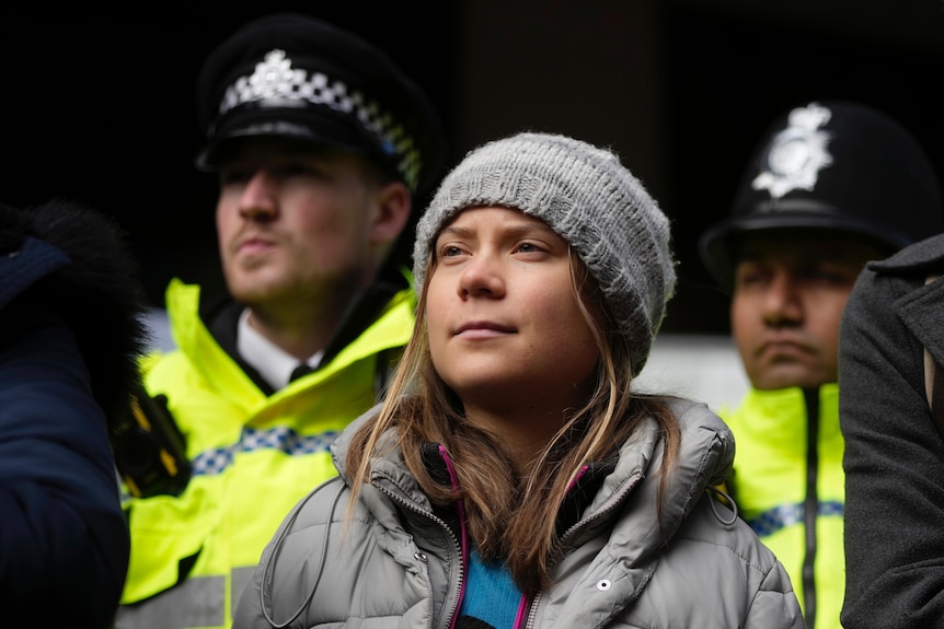 Greta Thunberg standing with a beanie on in front of UK police
