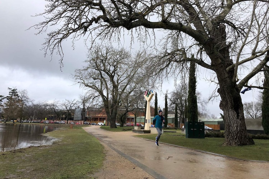 Julian Spence is dressed in a jacket, pants and a beanie as he runs around Lake Wendouree in Ballarat under grey skies.