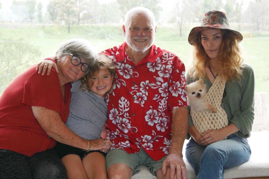 A foster family sit inside their home smiling, one year after bushfires destroyed property.