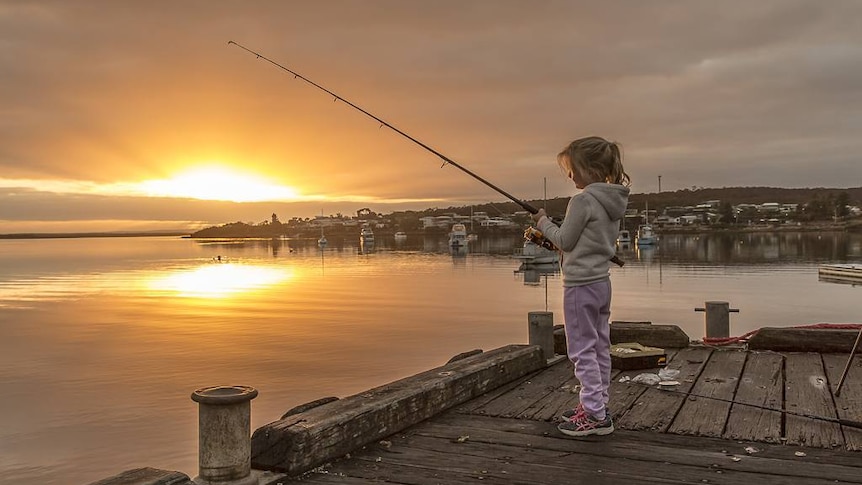 A girl tries to catch fish with her fishing rod off a jetty at Coffin Bay, South Australia.