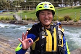 Woman in wetsuit and safety gear stands in front of fast flowing water