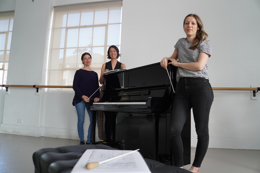 Three women pose around a grand piano.