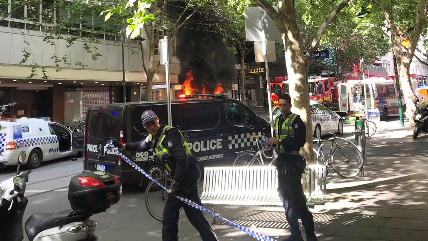 Victoria Police officers cordon off a road with flames in the background.