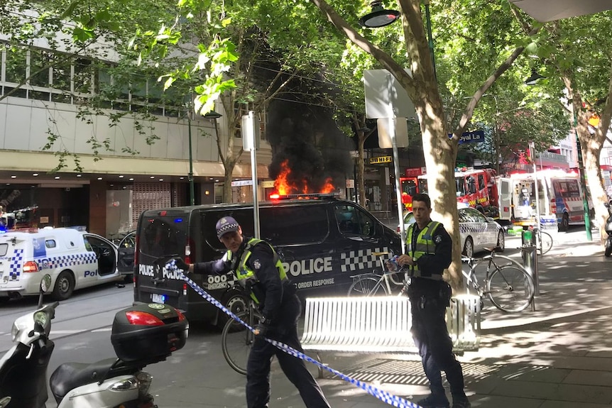 Victoria Police officers cordon off a road with flames in the background.