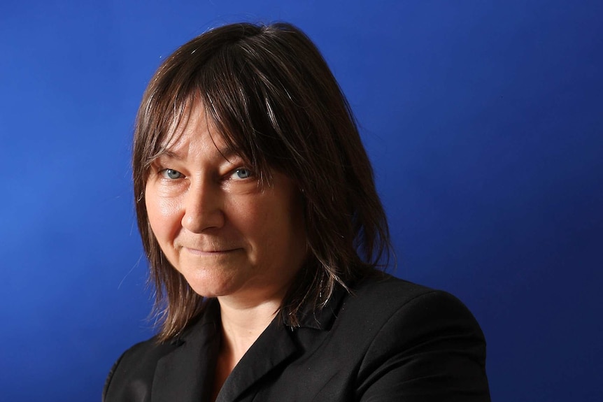 Colour wide photograph of author Ali Smith standing in blue backdrop.