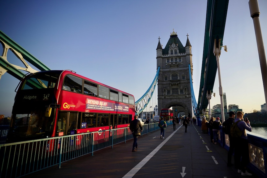 A red London double-decker bus crosses Tower Bridge.