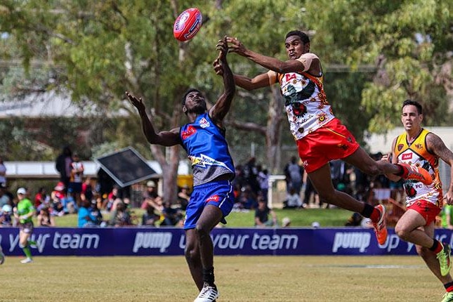 An AFL player in red and white uniform leaps for a mark above a player in blue.