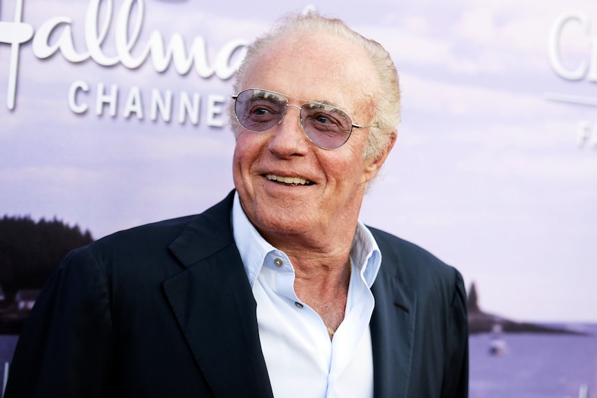 Close up of elderly man in suit wearing purple sunglasses on red carpet.