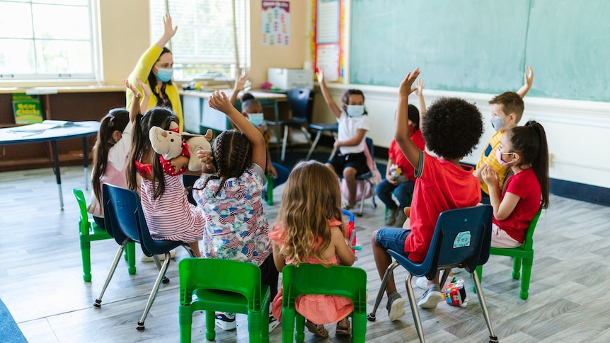 Children in a classroom with their teacher wearing masks.