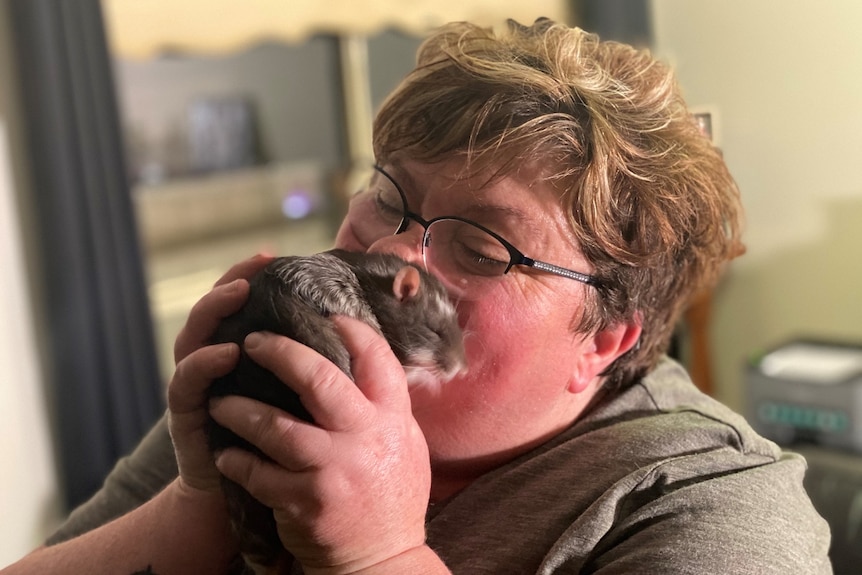 A woman holds a large rat up to her face and inhales deeply. She looks pleased.