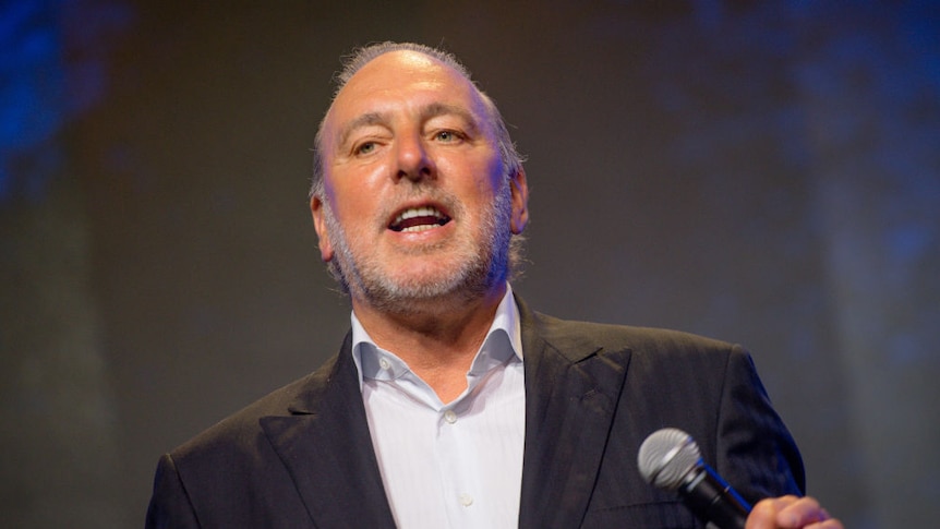 Brian Houston wearing a formal suit holding a microphone in his hand